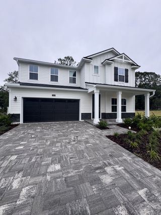 A modern white home with black accents and a paver driveway in Creighton Pointe by Drees Custom Homes (Fleming Island, FL).