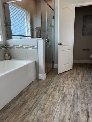 A modern bathroom featuring a glass shower, sleek bathtub, and wood-look flooring, creating a spa-like atmosphere.