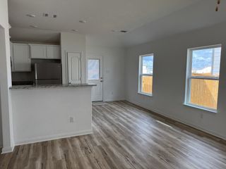 A bright, open living space with wood floors, granite breakfast bar, and ample natural light pouring through large windows.