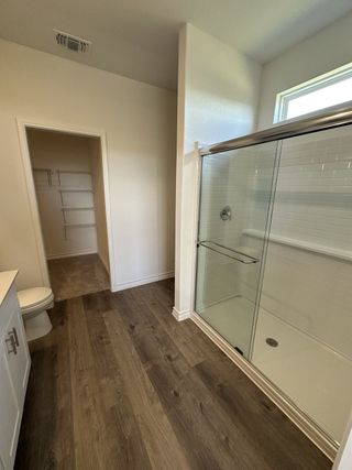 A modern bathroom with a glass-enclosed shower, wood-style flooring, and a spacious walk-in closet.
