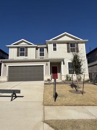 Street view A charming two-story home with gray siding and a red door in Saddleback at Santa Rita Ranch by Pulte Homes (Liberty Hill, TX).