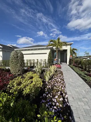 A beautiful white home with lush landscaping and palm trees in The Timbers at Everlands by Lennar (Palm Bay, FL).