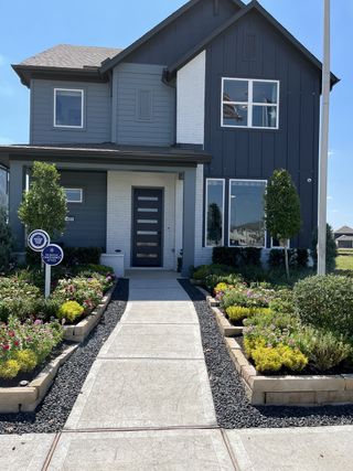 A modern gray and white home with a landscaped garden in Sienna by Chesmar Homes (Missouri City, TX).