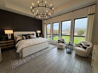Model Home A spacious bedroom featuring a luxurious bed, chic chandelier, elegant black accent wall, and large windows opening to a scenic view.