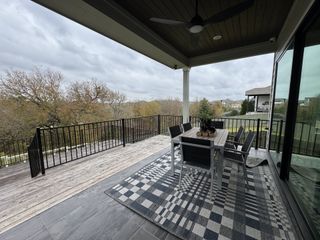 A cozy covered patio with a stylish dining set, checkered rug, and scenic views of nature, perfect for outdoor relaxation.