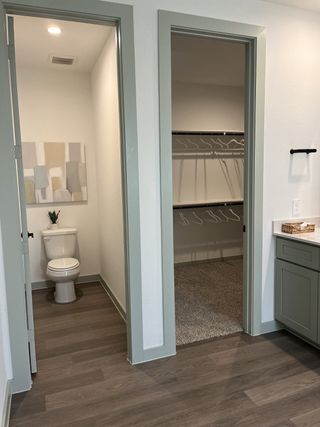 A modern bathroom featuring wood floors, a closet, and an adjacent toilet area with minimalist decor.