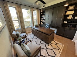 A sophisticated home office with a dark wood desk, modern shelving, large windows, and cozy seating.