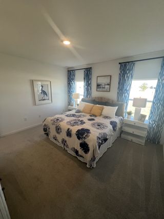 A cozy bedroom featuring a floral bedspread, patterned curtains, and soothing artwork on white walls.