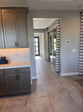 A modern hallway with light tiled floors, sleek cabinetry, and striped curtains leading to a bright entryway.