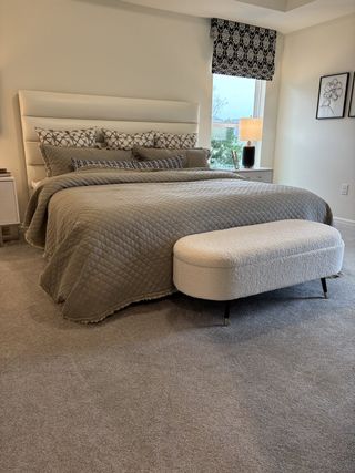 Model Home Elegant bedroom featuring a plush headboard, patterned pillows, and an ottoman. Cozy and modern decor with soothing tones.