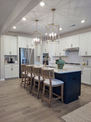 A modern kitchen featuring white cabinetry, a central island with seating, pendant lighting, and stainless appliances.