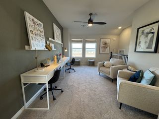 A cozy home office with a long desk, stylish artwork, plush seating, and soft carpeting illuminated by natural light.