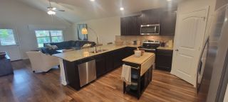 Model Home A modern kitchen with dark wood cabinets, granite countertops, and stainless steel appliances flows into a bright living area.