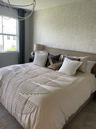 A serene primary bedroom with a textured accent wall, elegant bedding, and warm lighting in Tuscan Springs by Lennar (Pembroke Pines, FL).
