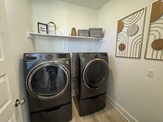 A modern laundry room featuring sleek appliances, wall art, and functional shelving with decor, creating a stylish and efficient space.