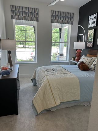 A cozy bedroom featuring large windows, athletic-themed décor, and plush carpeting for a comfortable ambiance.