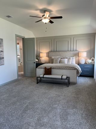 Model Home A cozy bedroom with a paneled accent wall, plush carpet, and elegant decor featuring soft lighting and a ceiling fan.