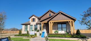 Street view A charming brick home with wood accents and lush landscaping in Alsatian Oaks: 50ft. lots by Highland Homes (Castroville, TX).