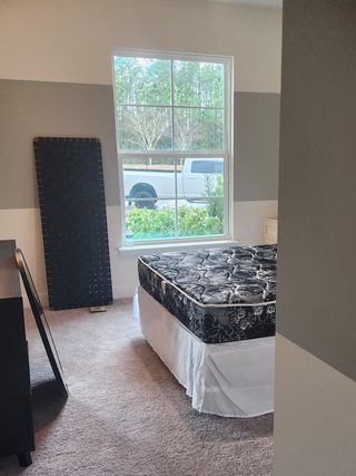 A cozy bedroom with soft carpeting, a large window, and a neatly made bed, offering serene and natural views.