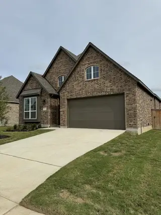 A classic brick home in VIDA by Highland Homes (San Antonio, TX) showcases a dark garage door, a bay window, and a well-maintained lawn.
