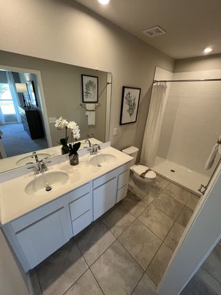 A sleek bathroom with dual sinks, large mirror, and a spacious shower, accented by elegant tile flooring and subtle decor.