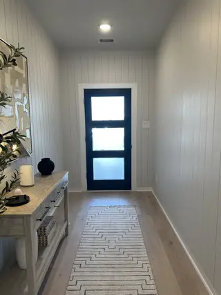 A modern entryway with sleek shiplap walls, a frosted glass door, and a chic console table on light wood flooring.