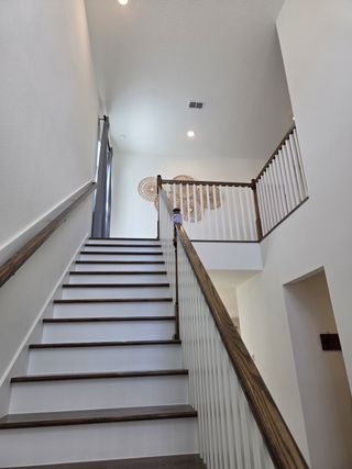 A bright, modern staircase with wooden steps and white railings, accentuated by woven wall art and ample natural light.