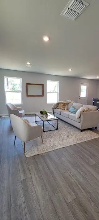 Model Home A cozy living room with elegant gray flooring, soft lighting, and modern furniture, including a comfy sofa and stylish chairs.