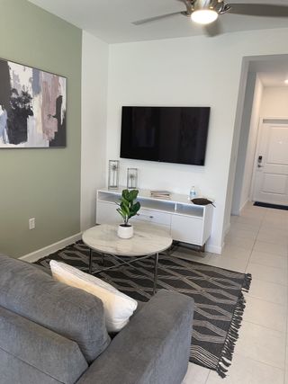 Cozy living area with a gray sofa, abstract art, and sleek TV setup, accented by a modern rug and greenery.