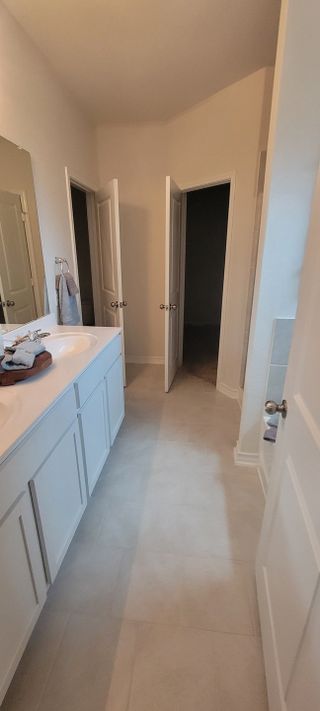 Model Home A bright bathroom with dual white vanities, light tile flooring, and separate doorways leading to a toilet room and closet.