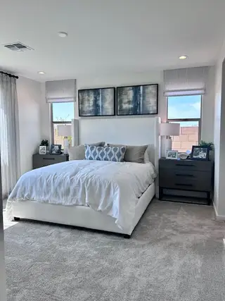 A serene bedroom featuring a plush white bed, modern art, and light-filled windows with elegant drapery.