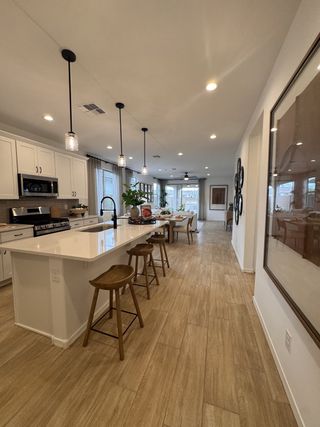 A modern kitchen with sleek white cabinetry, a spacious island, pendant lighting, and warm wood flooring.