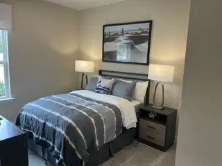 Model Home A cozy bedroom with modern lamps, abstract art, and a plush bed featuring chic grey and white bedding.