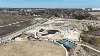 An aerial view of Lisso by Taylor Morrison in Pflugerville, TX, showcasing a sports field, playground, tennis court, and undeveloped land, highlighting community amenities.