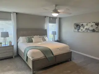 A serene bedroom featuring a wooden bed, soft neutral tones, modern ceiling fan, and elegant floral artwork.