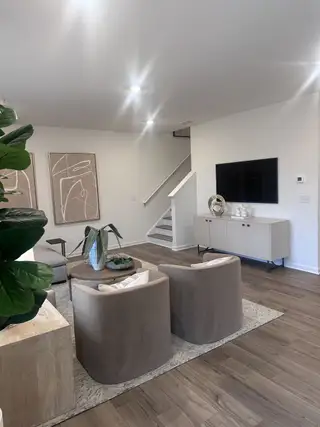 A modern living area with sleek furniture, abstract art, and cozy lighting, featuring stylish wood flooring and a large TV.