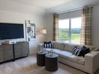 A cozy living room with a beige sectional, patterned pillows, abstract art, and panoramic window views of greenery.