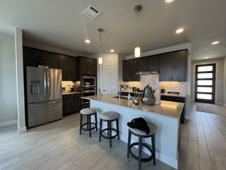 A modern kitchen featuring dark cabinetry, a sleek island with bar stools, stainless steel appliances, and chic lighting.