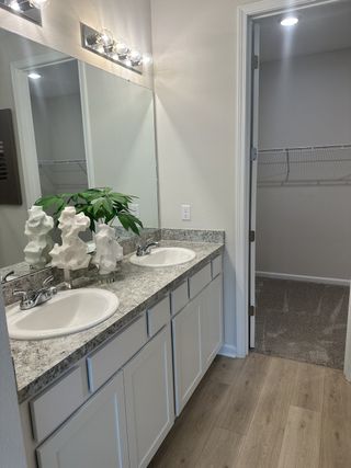 Model Home A bright bathroom with dual sinks, granite countertop, and sleek lighting leads to a walk-in closet.