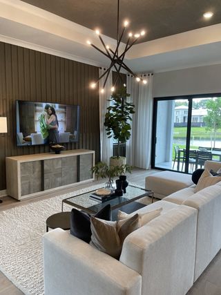 A modern living room with a sleek chandelier, neutral tones, and large sliding doors opening to an outdoor space.