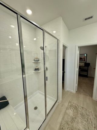 A modern bathroom shower with sleek glass doors, white subway tiles, and recessed lighting, creating a bright and clean space.