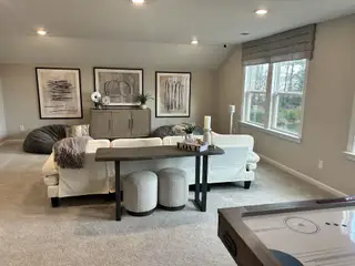 A cozy living room with neutral decor, plush seating, abstract art, and ample natural light from large windows.