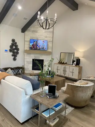 Model Home A cozy living room with a stone fireplace, modern chandelier, and stylish decor, featuring neutral tones and rustic wood accents.