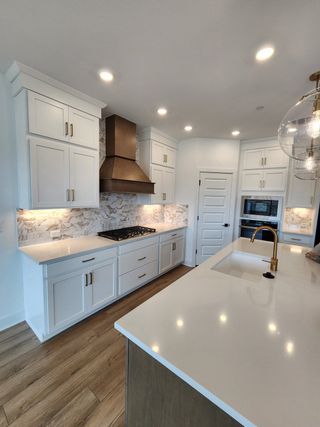 Model Home A modern kitchen featuring sleek white cabinets, a marble backsplash, and a stylish bronze hood.