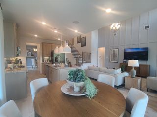 An open-concept living space with elegant kitchen, cozy seating, and modern lighting features a wooden dining table centerpiece.