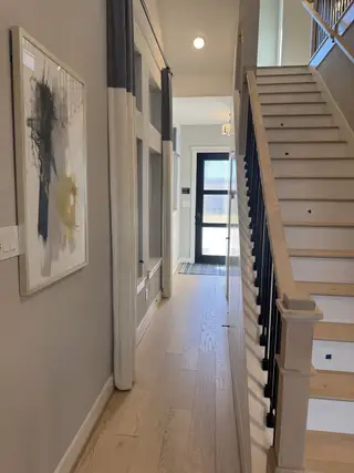 Model Home A modern hallway with light wood flooring, abstract art, and sleek staircase railing. Bright natural light filters from the entrance.
