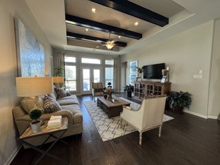 A cozy living room with dark wood floors, beige sofa, rustic TV console, and exposed beam ceiling.