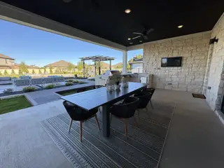 Model Home A stylish covered patio with a sleek dining set, outdoor kitchen, and spacious lawn area. Perfect for entertaining and relaxation.