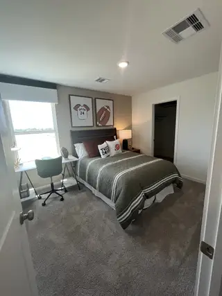 A cozy bedroom with sports-themed decor, a soft carpet, and a functional desk by the window for studying.