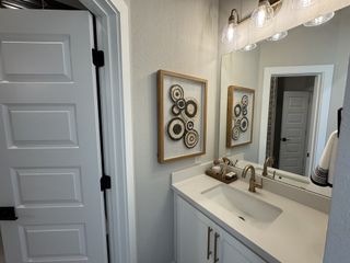Model Home A chic bathroom with elegant fixtures, a sleek white vanity, and artistic circular wall decor.